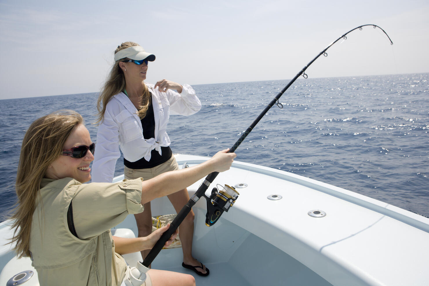 Two women are fishing on the bow of a boat with the rod bending on a catch.