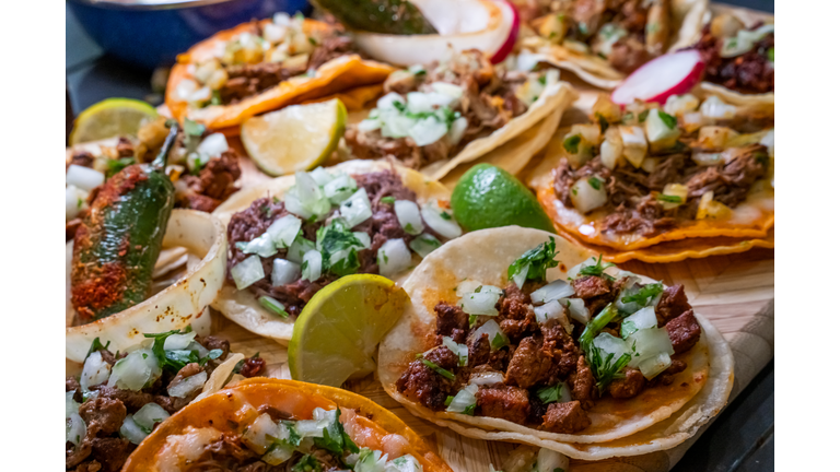 Assortment Of Delicious Authentic Tacos, Birria, Carne Asada, Adobada, Cabeza And Chicharone, Arranged With Lime Slices, Onion, And Roasted Chili Pepper