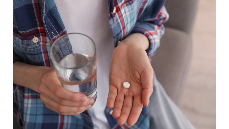 Young woman with abortion pill and glass of water indoors, closeup