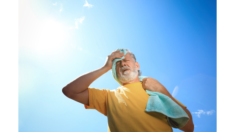 Senior man with towel suffering from heat stroke outdoors, low angle view