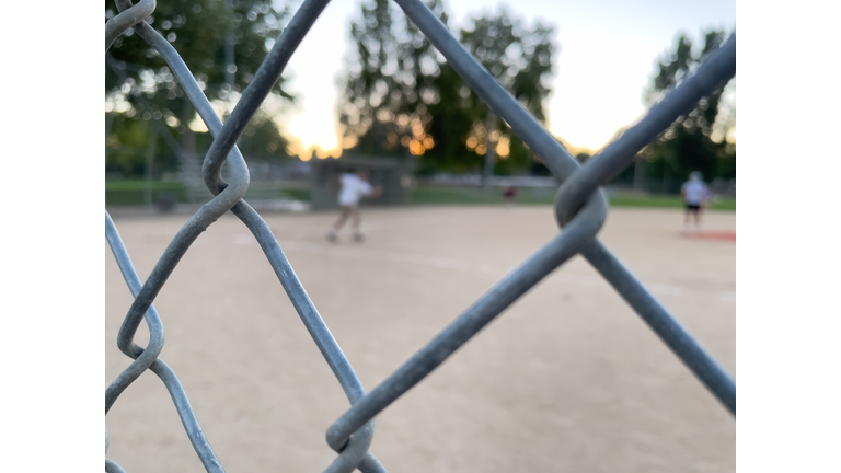 Looking through chainlink fence at baseball game in the evening. Chainlink fence is in focus. People on field are out of focus