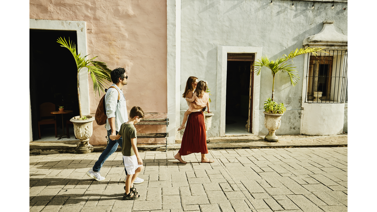 Wide shot of family walking down street while exploring town during vacation