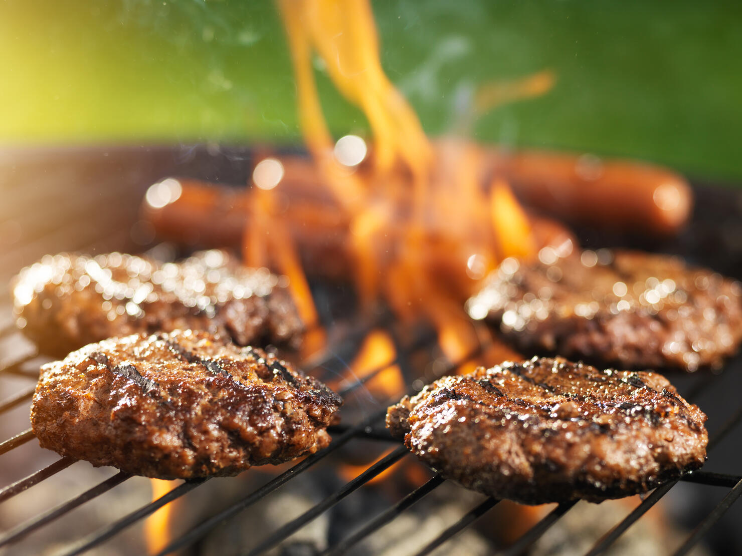 hamburgers and hotdogs cooking on flaming grill