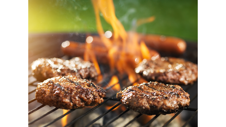 hamburgers and hotdogs cooking on flaming grill