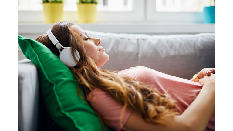 Portrait of a beautiful young woman lying on sofa with headphones on and closed eyes, relaxing