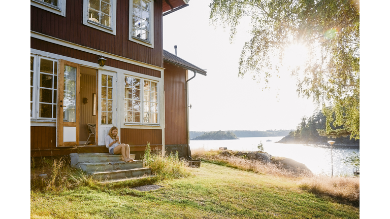Woman using phone while sitting on steps in doorway of log cabin