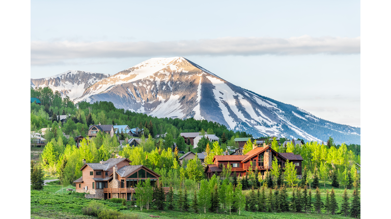 Mount Crested Butte, Colorado village in summer with colorful sunrise by wooden lodging houses on hills with green trees