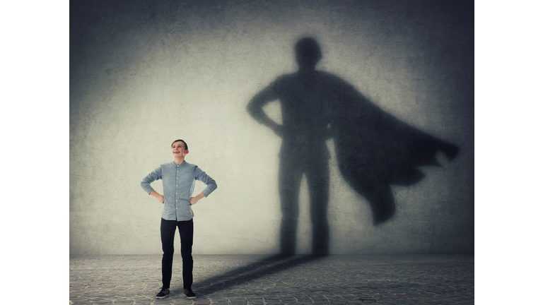 Casual teenage, keeps arms on hips smiling confident, casting a superhero with cape shadow on the wall. Student ambition success concept. Leadership hero power, motivation and inner strength symbol.