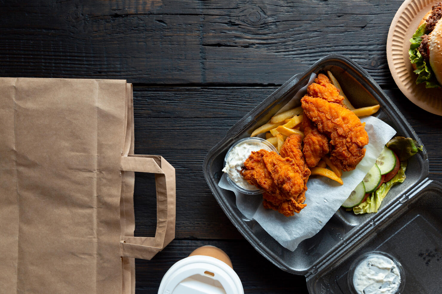 Hamburger, french fries and fried chicken in takeaway containers on the wooden background. Food delivery and fast food concept