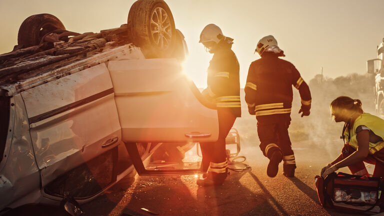 Car Crash Traffic Accident: Paramedics and Firefighters Plan Rescuing Passengers Trapped in Rollover Vehicle. Medics Prepare Stretchers and First Aid Equipment. Firemen Use Hydraulic Cutters Spreader