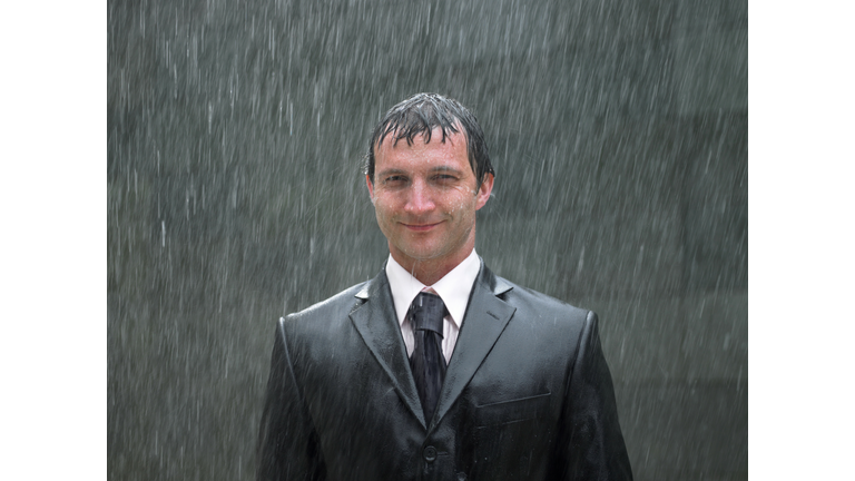 Businessman standing in rain, smiling, portrait, close-up