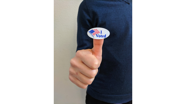 Young Male voter holding up a "I voted" sticker on his thumb