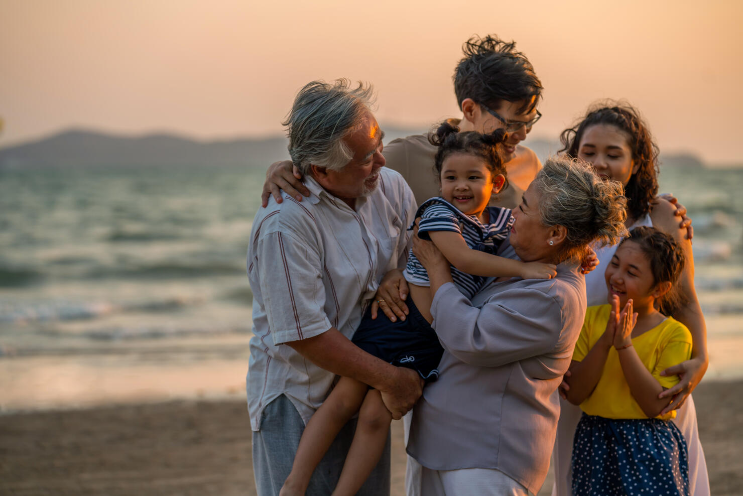 Multi-generation Asian family holding hands and walking together on the beach at summer sunset