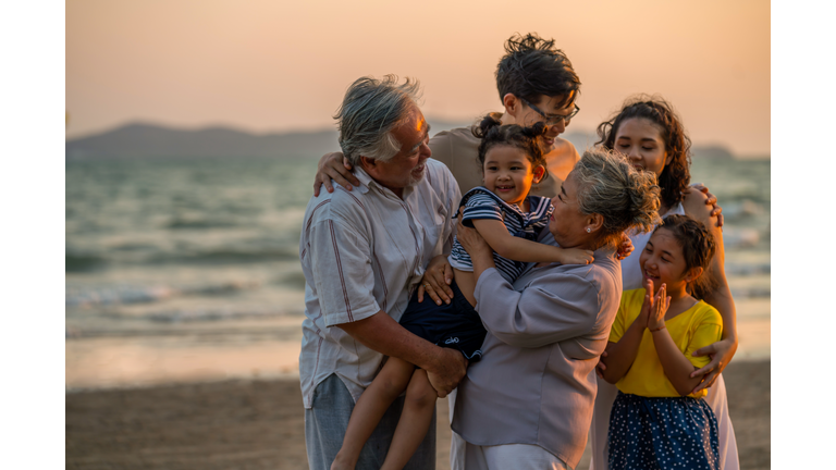 Multi-generation Asian family holding hands and walking together on the beach at summer sunset