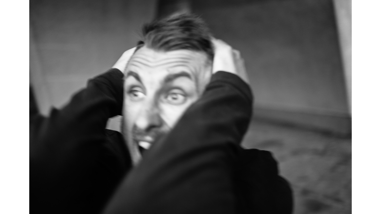 Close-up black and white portrait of a young bearded man who grabbed his hair and screams in despair looking into the void. His expression is full of despair, heartache, regret, rejection and anger.