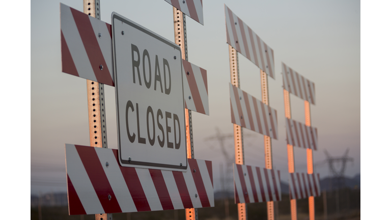 Road closed sign on barricade against sky during sunset