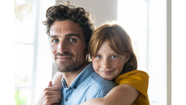 Smiling redhead daughter with blue eyes cuddling father in living room