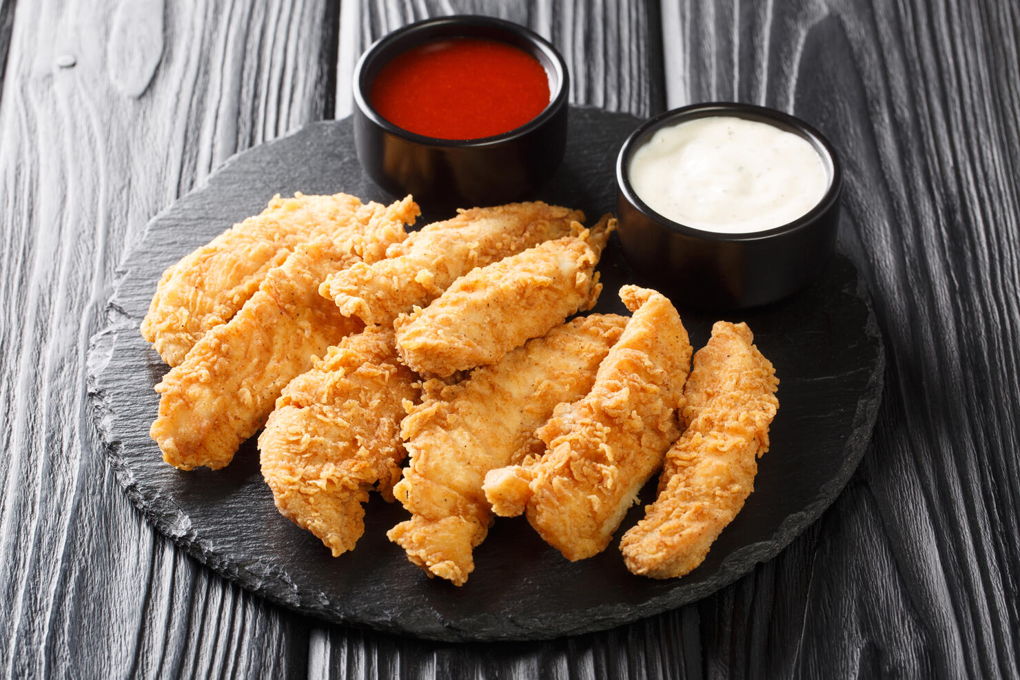 Chicken strips with tomato sauce and mayonnaise closeup. Fast food on black background. Horizontal