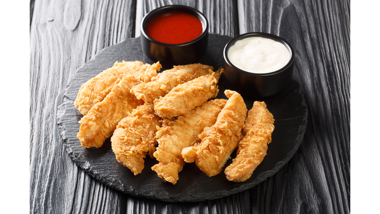 Chicken strips with tomato sauce and mayonnaise closeup. Fast food on black background. Horizontal