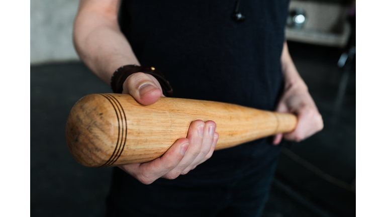 A wooden baseball bat in the hands of a man or a teenage boy, a student. The concept of sports play and leisure, entertainment and competitions, self-defense, defense and protection.
