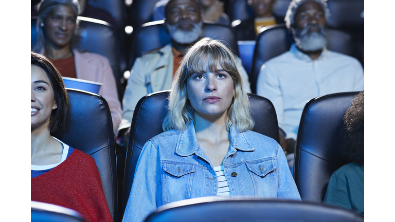 Young blond woman watching movie with smiling friend in theater