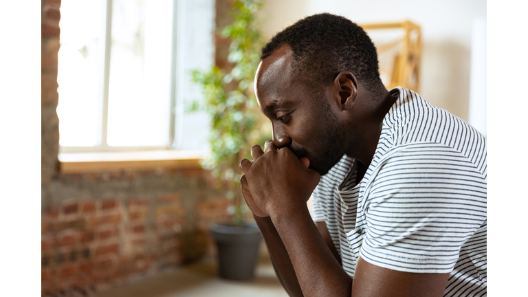 Portrait of young sad african man sitting and thinking about personal problems. Side view