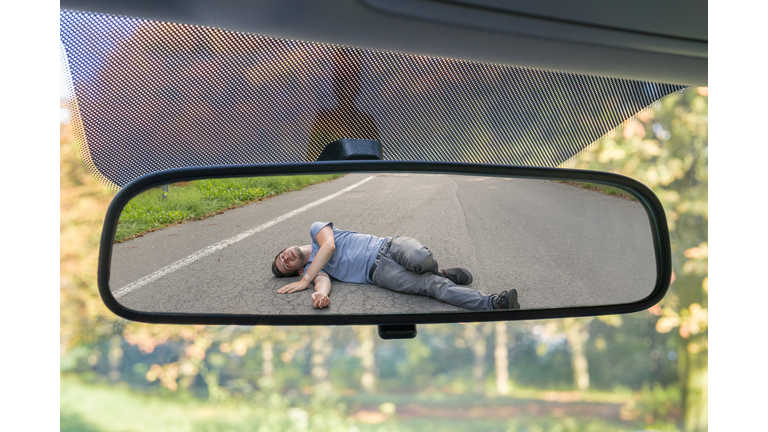 Hit and run concept. View on injured man on road in rear mirror of a car.