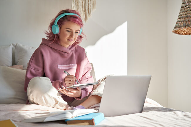 Hipster teen girl student with pink hair watch online webinar learning in bed.