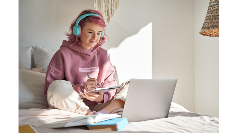 Hipster teen girl student with pink hair watch online webinar learning in bed.