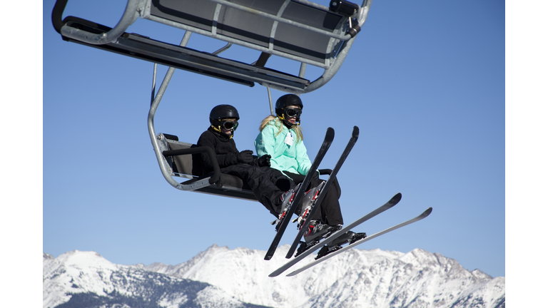 Two skiers ride ski lift to top of mountain. Sky.