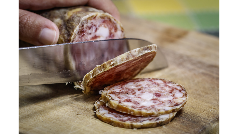 Artisanal Friulian salami being sliced on a rustic wooden cutting board