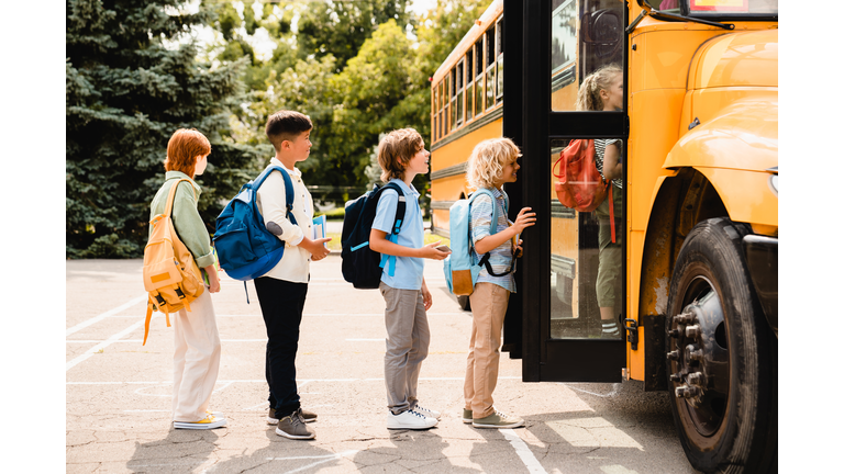 Multiethnic mixed-race pupils classmates schoolchildren students standing in line waiting for boarding school bus before starting new educational semester year after summer holidays