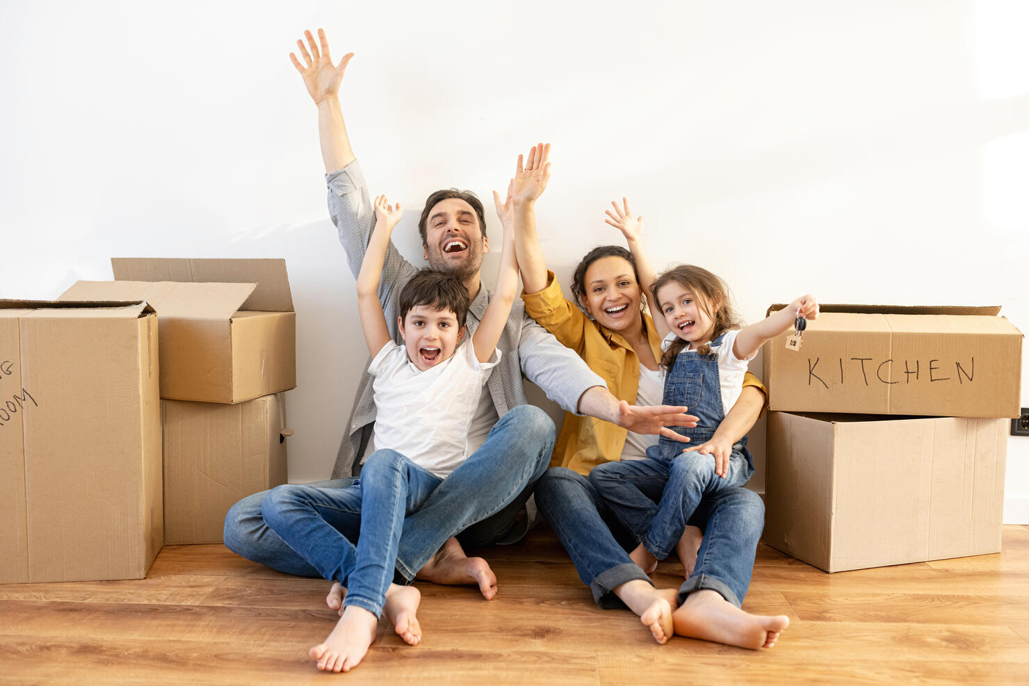 Overjoyed multiracial family of four sitting on floor surrounded cardboard boxes