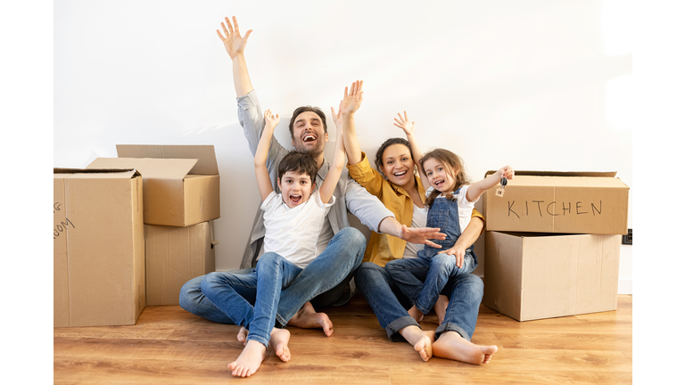 Overjoyed multiracial family of four sitting on floor surrounded cardboard boxes