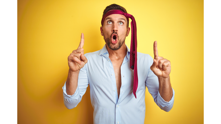 Hangover business man drunk and crazy for hangover wearing tie on head amazed and surprised looking up and pointing with fingers and raised arms.