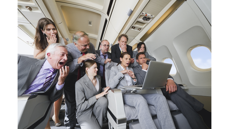 Germany, Bavaria, Munich, Group of passengers looking in laptop in business class airplane cabin