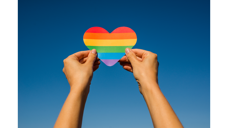 Woman holds in hands a heart in the colors of the rainbow. Young beautiful girl. LGBT history month. Pride Month. Lesbian Gay Bisexual Transgender. LGBT flag. Love, human rights, tolerance. LGBTQ+
