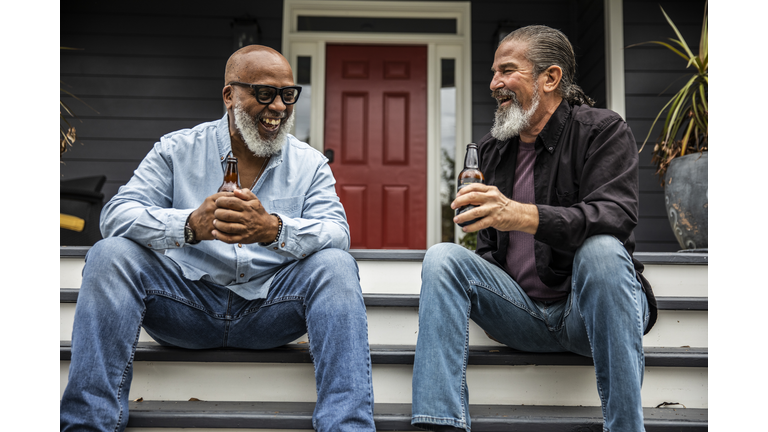 Senior men having beers and talking on front porch