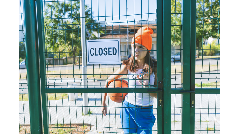 Teenage girl standing behind closed  playground door with Closed sign