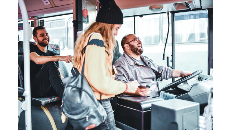 Bus Driver Joking With Young Female Paying For Ticket With Credit Card