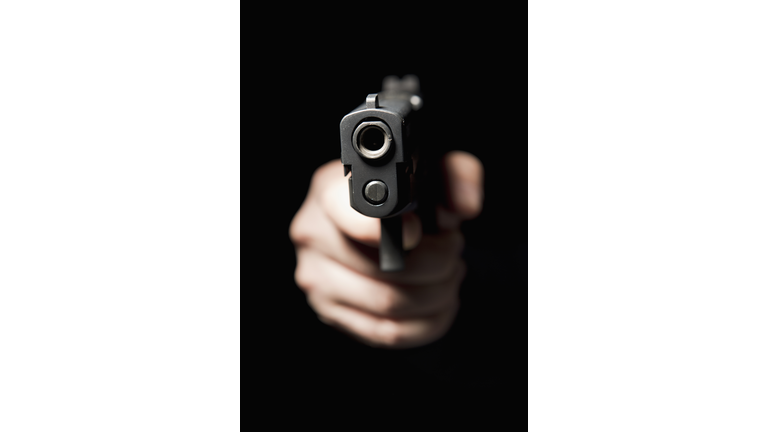 A hand holding a gun and pointing it at the camera, black background