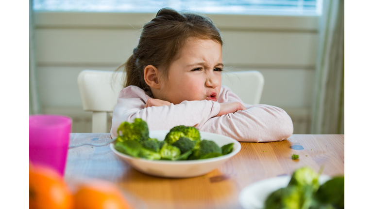 Cute girl eating spinach and broccoli at the table