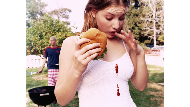 Teenage girl (16-18) looking at  ketchup stains on white dress