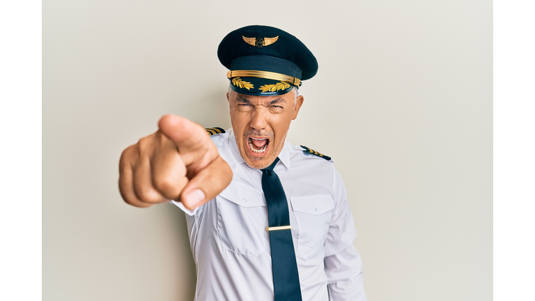 Handsome middle age mature man wearing airplane pilot uniform pointing displeased and frustrated to the camera, angry and furious with you