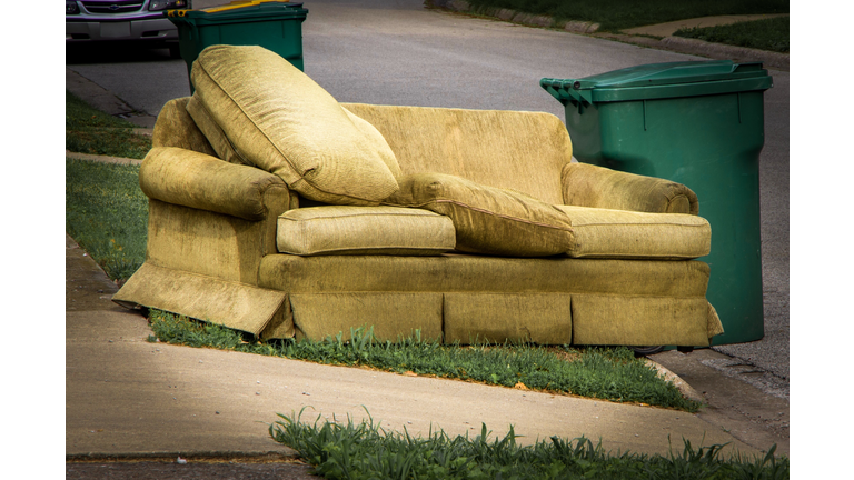 Old couch sitting along curb beside garbage container on trash day