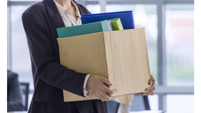 business concept:   An unemployed with her cardboard box walking out of the work office.