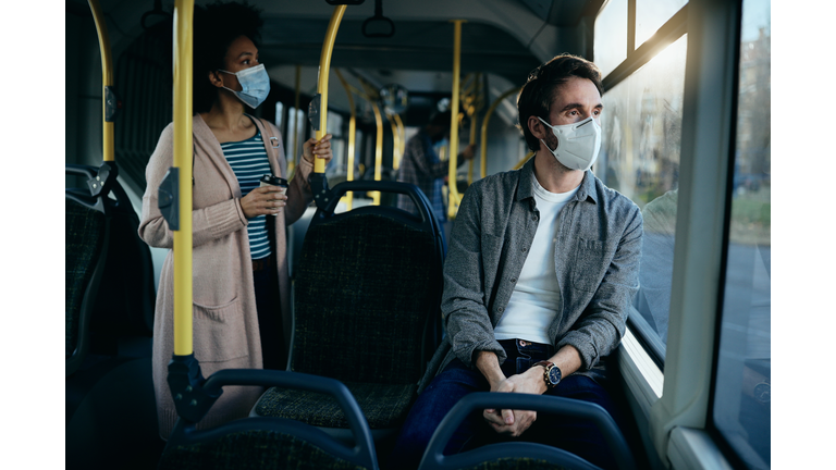 Pensive man with face mask commuting by bus and looking through the window.