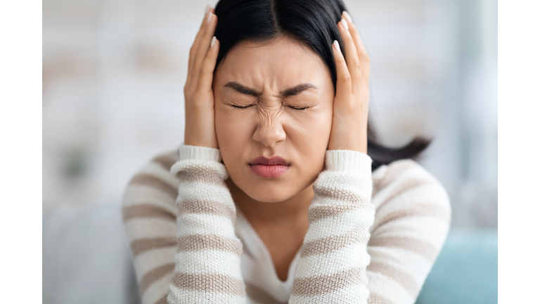 Emotional Asian Woman Covering Ears With Hands At Home