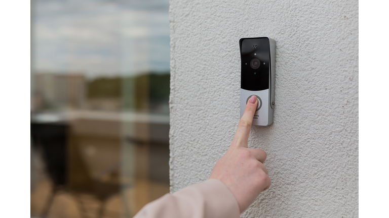 woman's hand uses a doorbell on the wall of the house with a surveillance camera