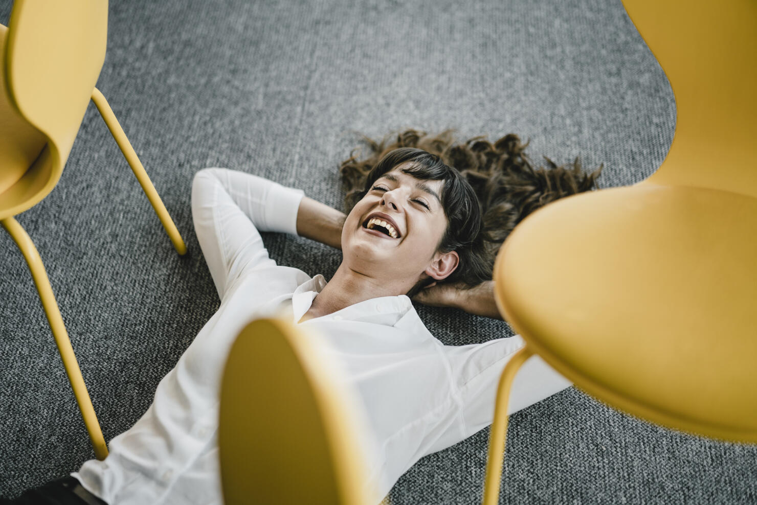 Laughing businesswoman laying in an office on the floor between chairs